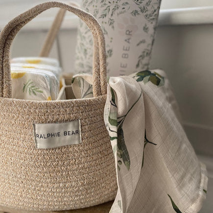 Woven basket with baby items including a blanket and a bottle, branded 'Ralphie Bear'.