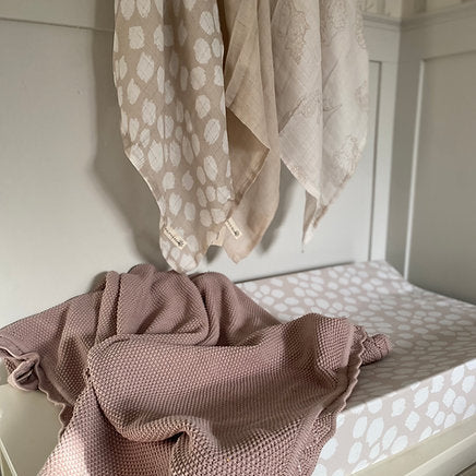 Pink textured blanket on a white surface with patterned fabric in the background