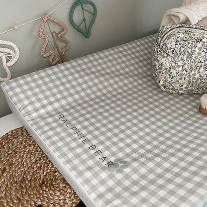 Checkered crib sheet with 'Ralphie Bear' branding on a crib, surrounded by decorative items.