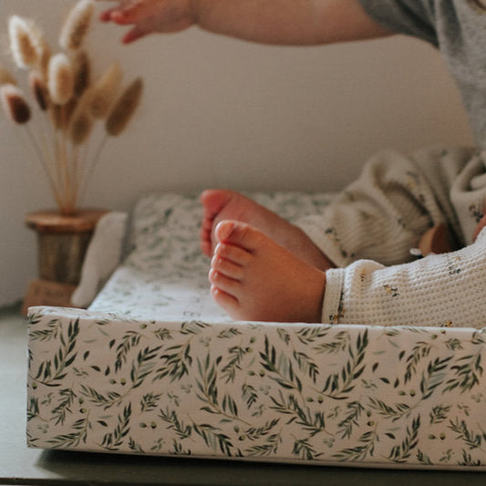 Person lying on a bed with a floral-patterned mattress cover, next to a small plant.