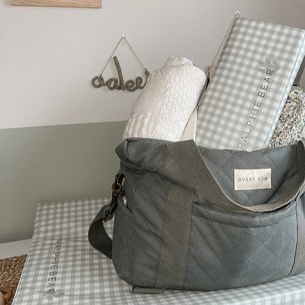 Gray bag with a checkered blanket and baby items on a bed, with 'Ralph Bear' branding.