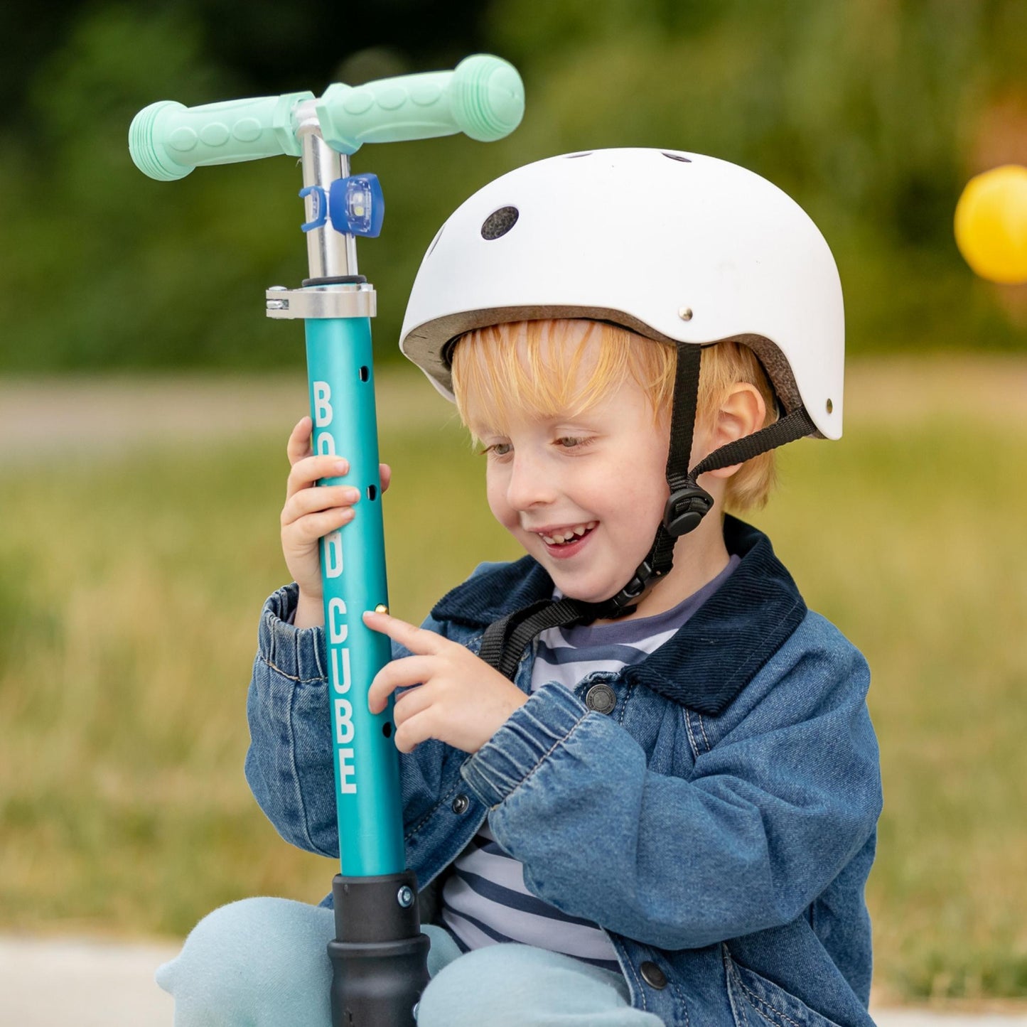 Child holding a blue scooter with a helmet outdoors