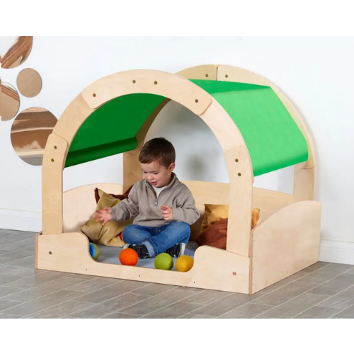Child playing inside a wooden playhouse with a green roof on a tiled floor.