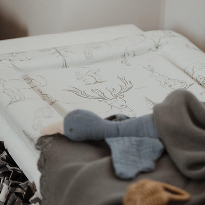 Baby crib with white mattress featuring deer patterns and a gray elephant toy.