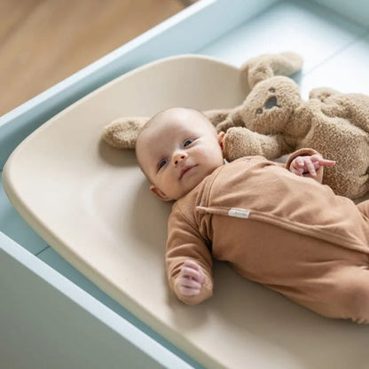 Baby lying on a changing table with a brown teddy bear