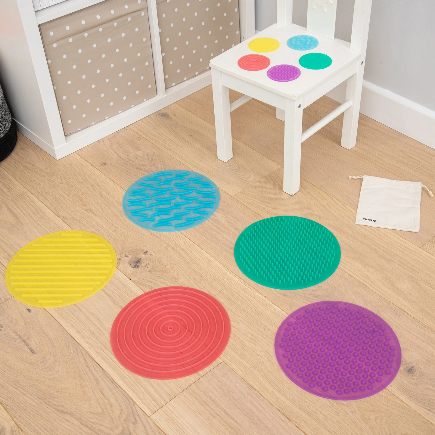Colourful round sensory mats on a wooden floor with a white chair.