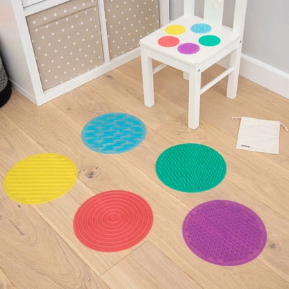 Colourful round sensory mats on a wooden floor with a white chair.