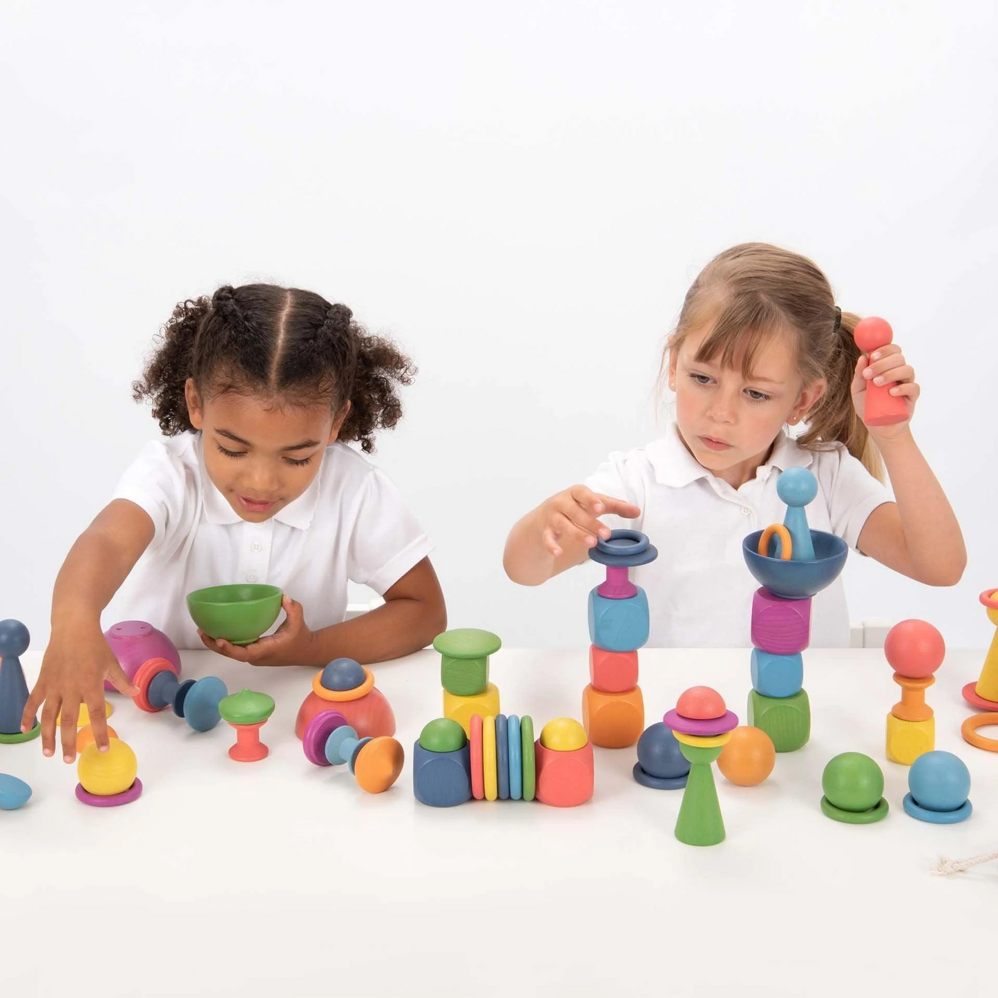 Two children playing with wooden rainbow loose parts.