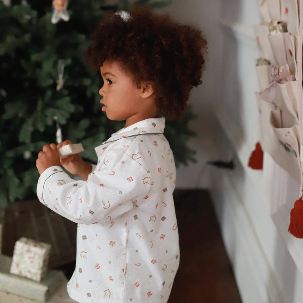 Child in a white shirt with patterns standing in front of a decorated Christmas tree.
