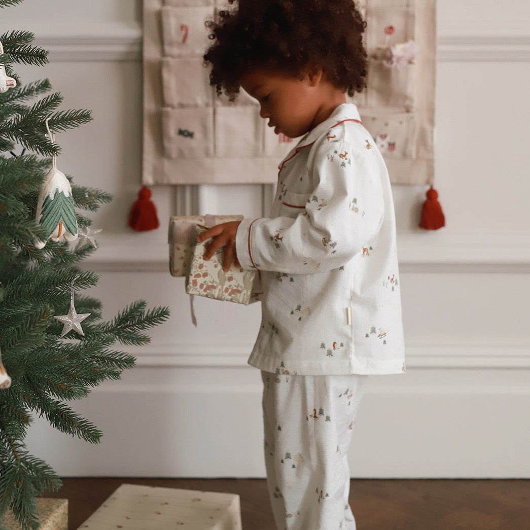 Child in pajamas holding a gift near a decorated Christmas tree.