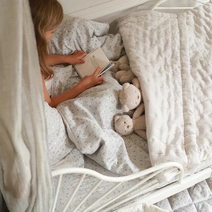 Child reading a book in bed with teddy bears and soft bedding