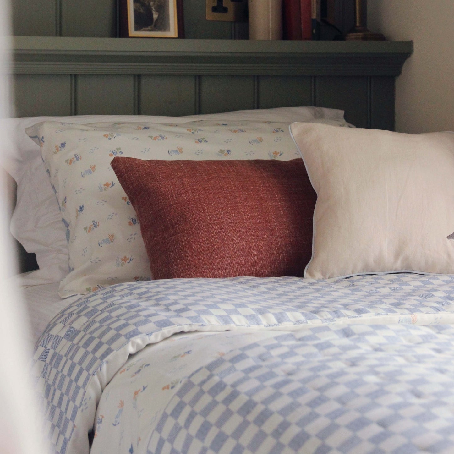 Bed with patterned bedding and pillows against a wooden headboard.