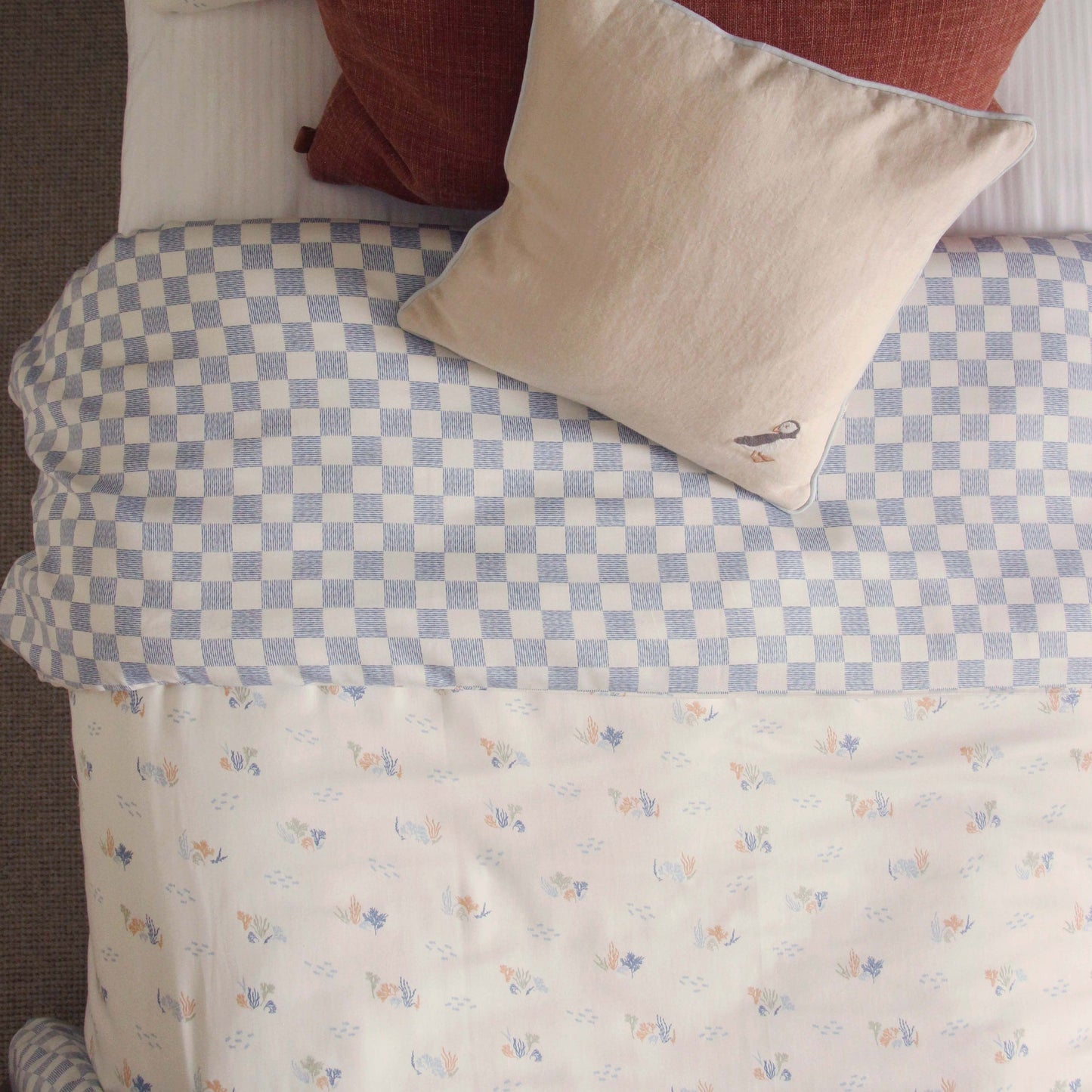 Bed with checkered blue and white duvet and floral-patterned bedspread