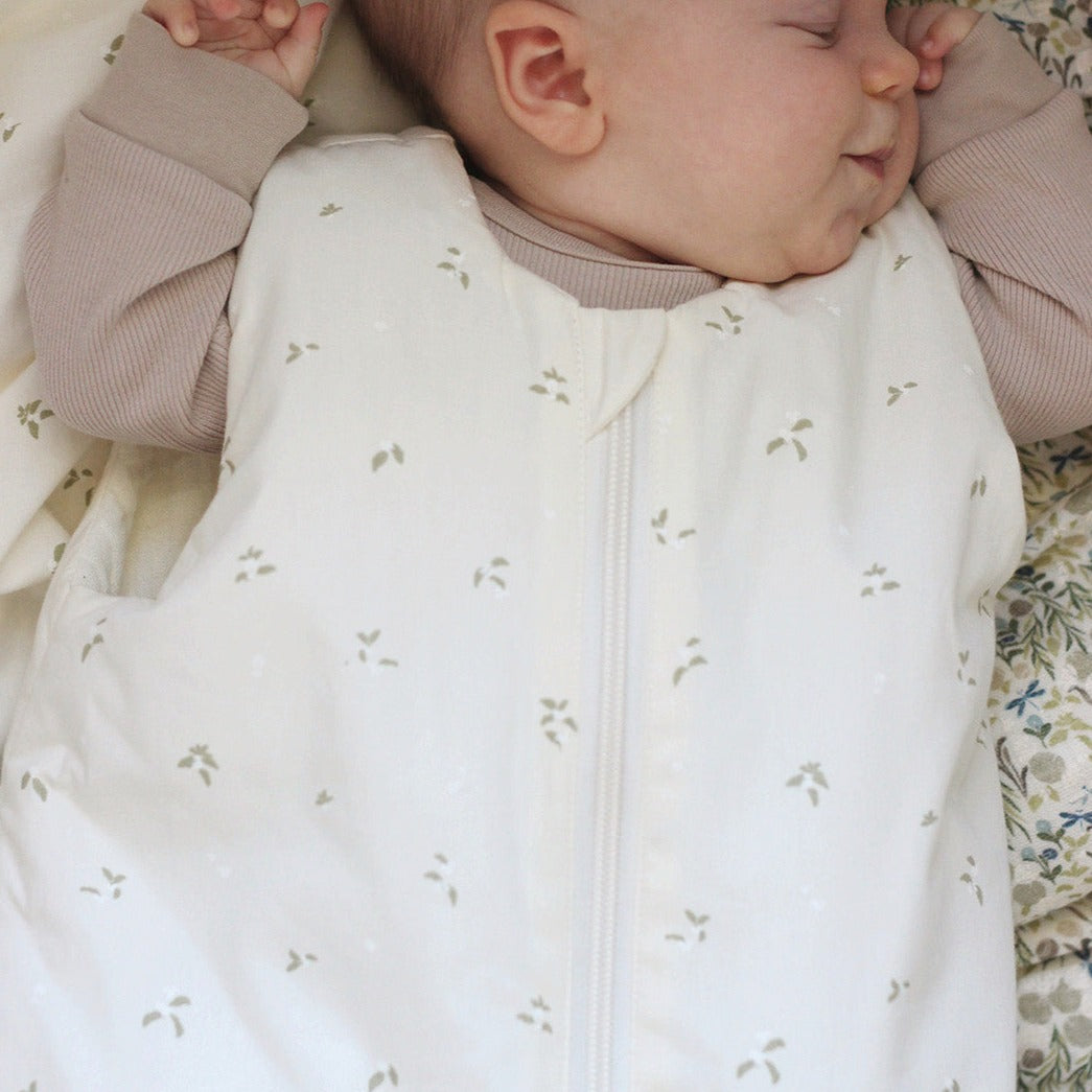 Baby sleeping in a white sleep bag with small patterns, wearing a beige outfit.