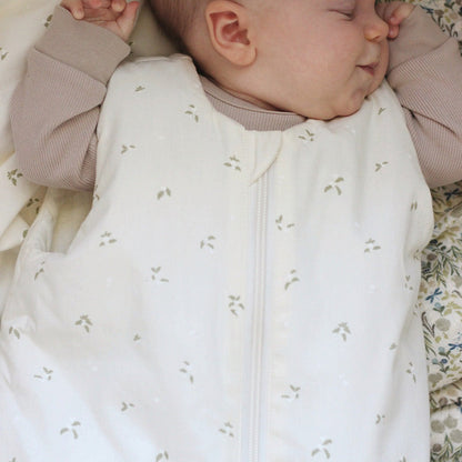 Baby sleeping in a white sleep bag with small patterns, wearing a beige outfit.