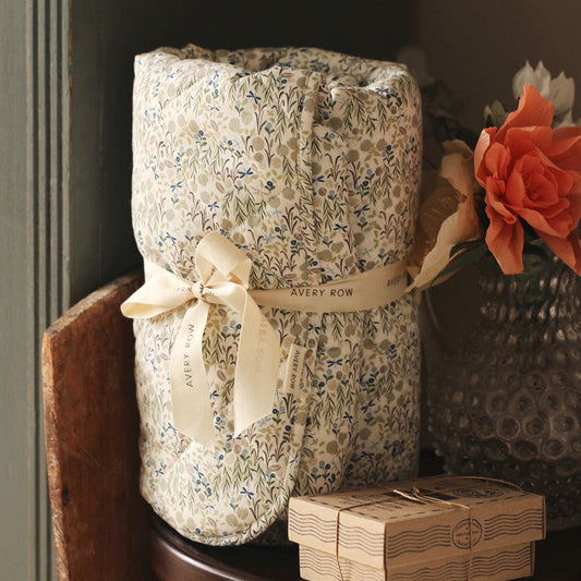 Floral-patterned gift bag with a ribbon and 'Avery Row' branding, placed on a wooden surface with a vase of flowers in the background.