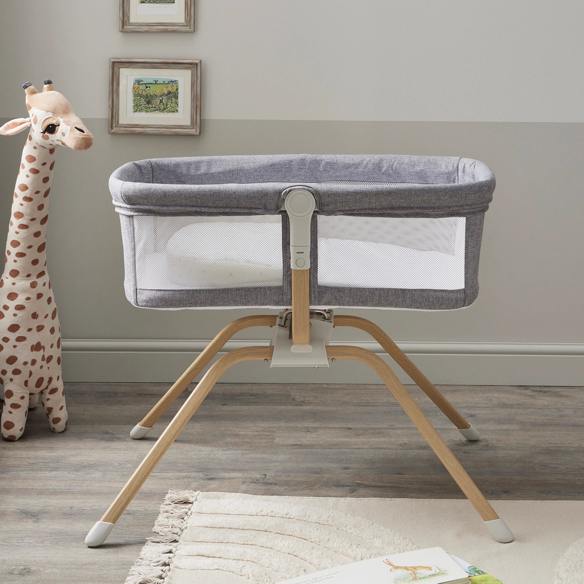 Portable crib on a stand in a room with a stuffed giraffe and framed pictures on the wall.