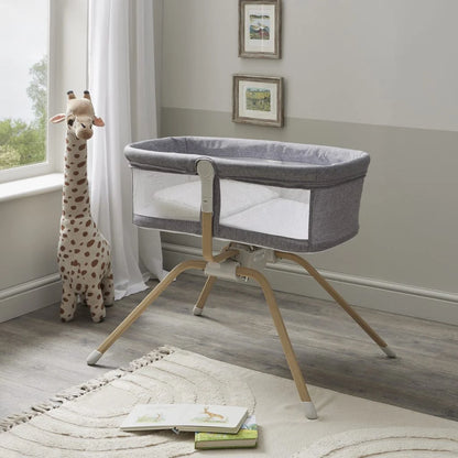 Gray baby crib with wooden legs in a room with a giraffe toy and books on a rug.