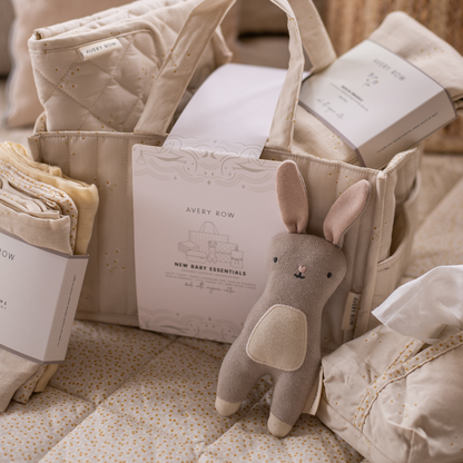 Baby essentials set with a plush rabbit toy, folded blankets, and a basket labeled 'Avery Row' on a soft surface.
