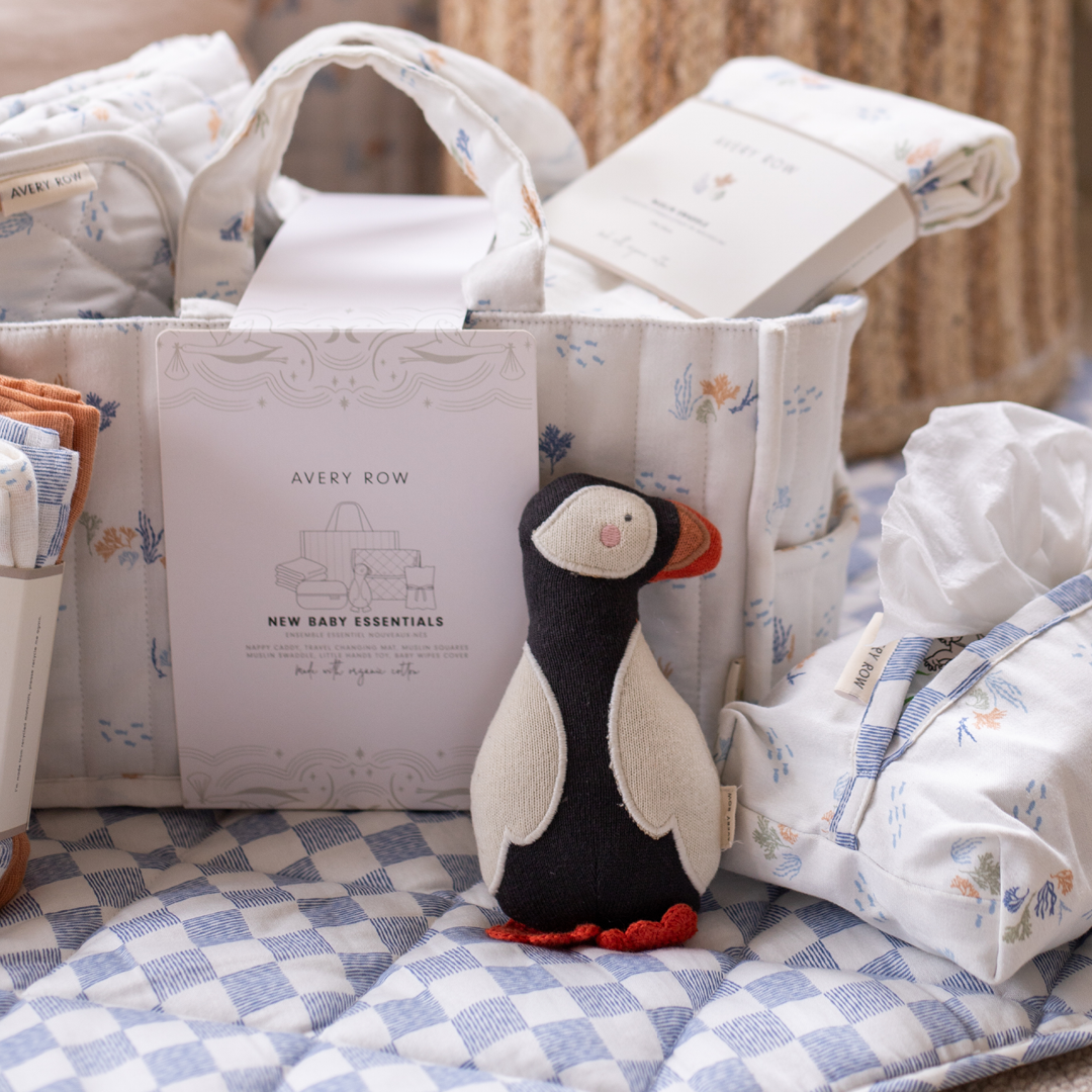 Baby essentials basket with a plush penguin toy on a checkered blanket