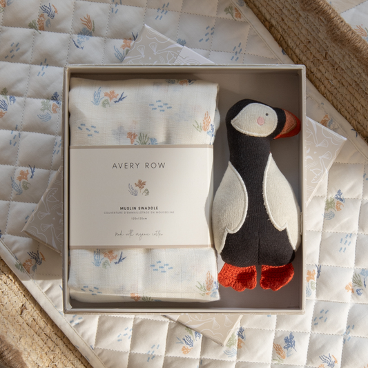 Baby gift set with swaddle and plush toy in a box on a quilted surface