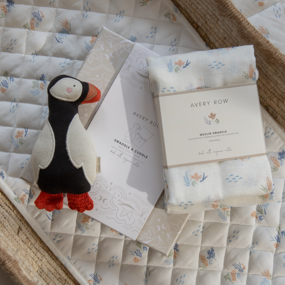 Baby swaddle blanket with puffin toy and Avery Row packaging on a quilted surface