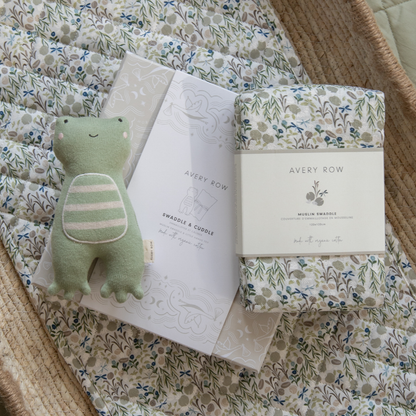 Floral swaddle blanket with a green plush toy and Avery Row packaging on a textured surface.