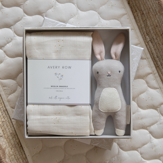 Baby gift set with swaddle and toy in a box on a textured surface