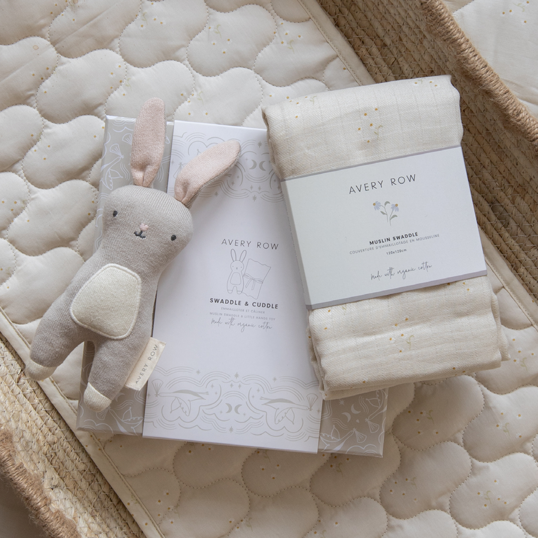 Baby gift set with plush bunny, book, and swaddle blanket on a textured surface