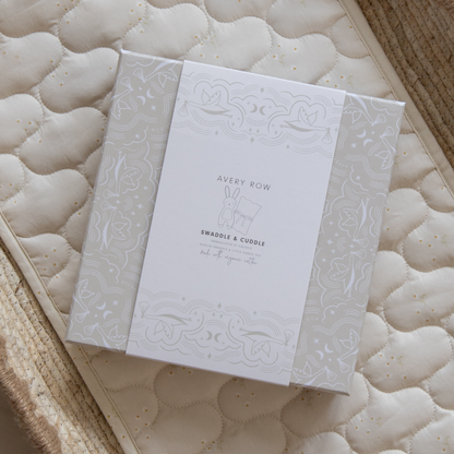 White baby swaddle and cuddle blanket with 'Avery Row' branding on a textured surface.