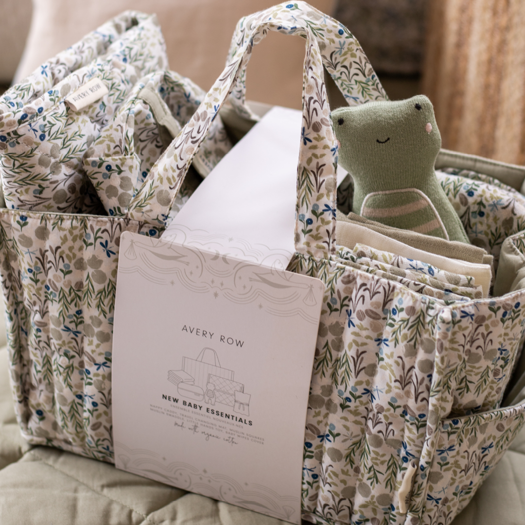 Floral-patterned baby caddy with baby items including a book and plush toy on a beige surface.