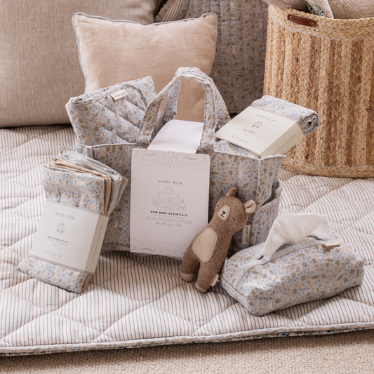 Baby essentials including a blanket, books, and a plush toy on a quilted surface.