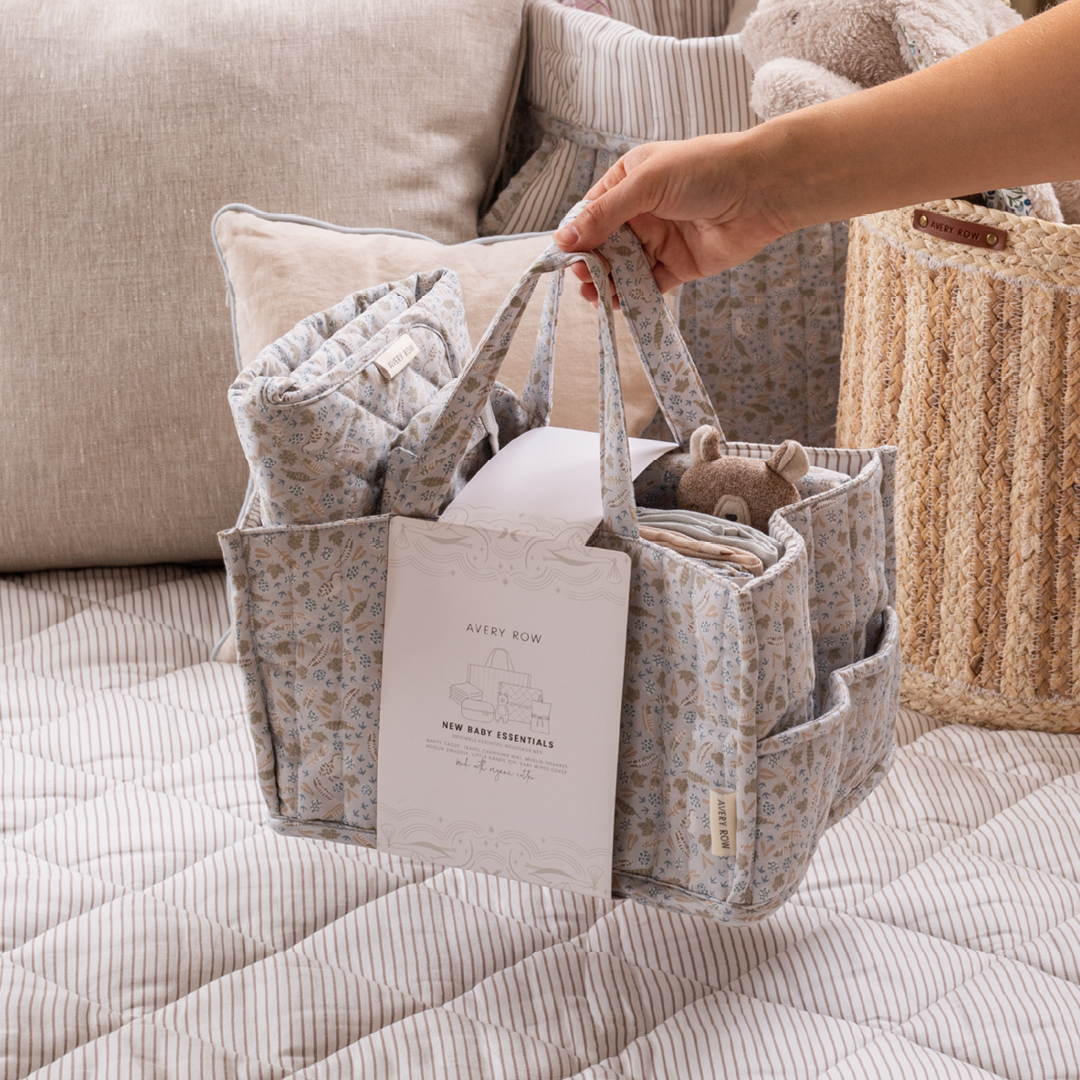Baby essentials in a floral-patterned bag held by a hand on a soft surface.
