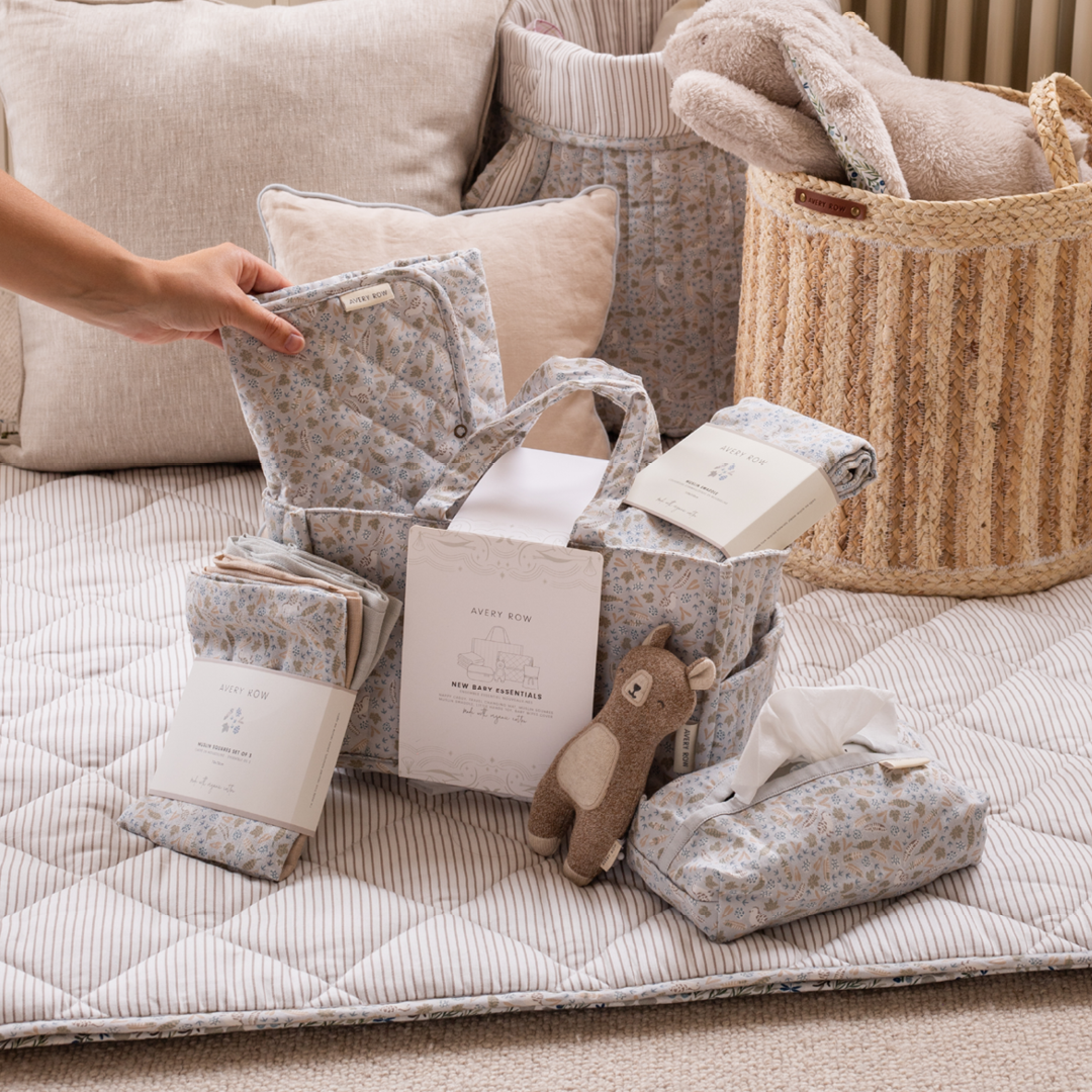 Baby products including pillows, blankets, and a toy on a quilted surface with baskets in the background.