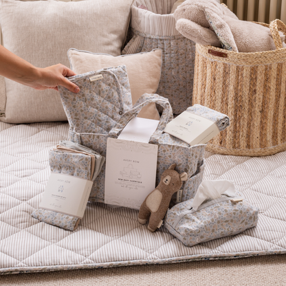 Baby products including pillows, blankets, and a toy on a quilted surface with baskets in the background.