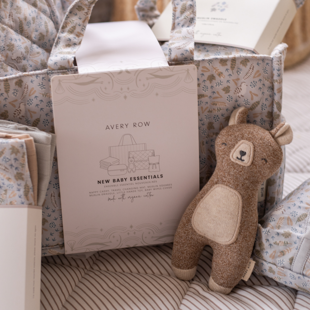Baby gift set with plush toy, blanket, and book labeled 'Avery Row' on a floral-patterned surface.