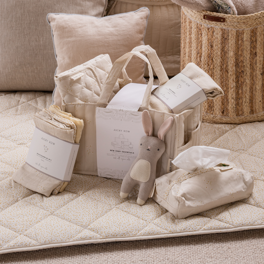 Baby care products including a plush toy, diapers, and a basket on a quilted surface.