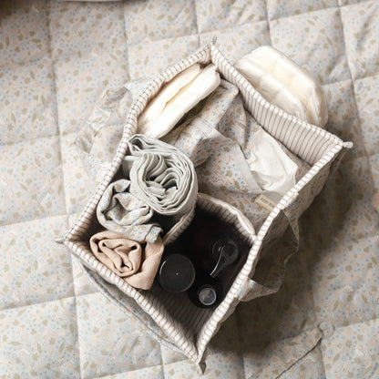 Folded clothes and a black item in a woven basket on a quilted surface