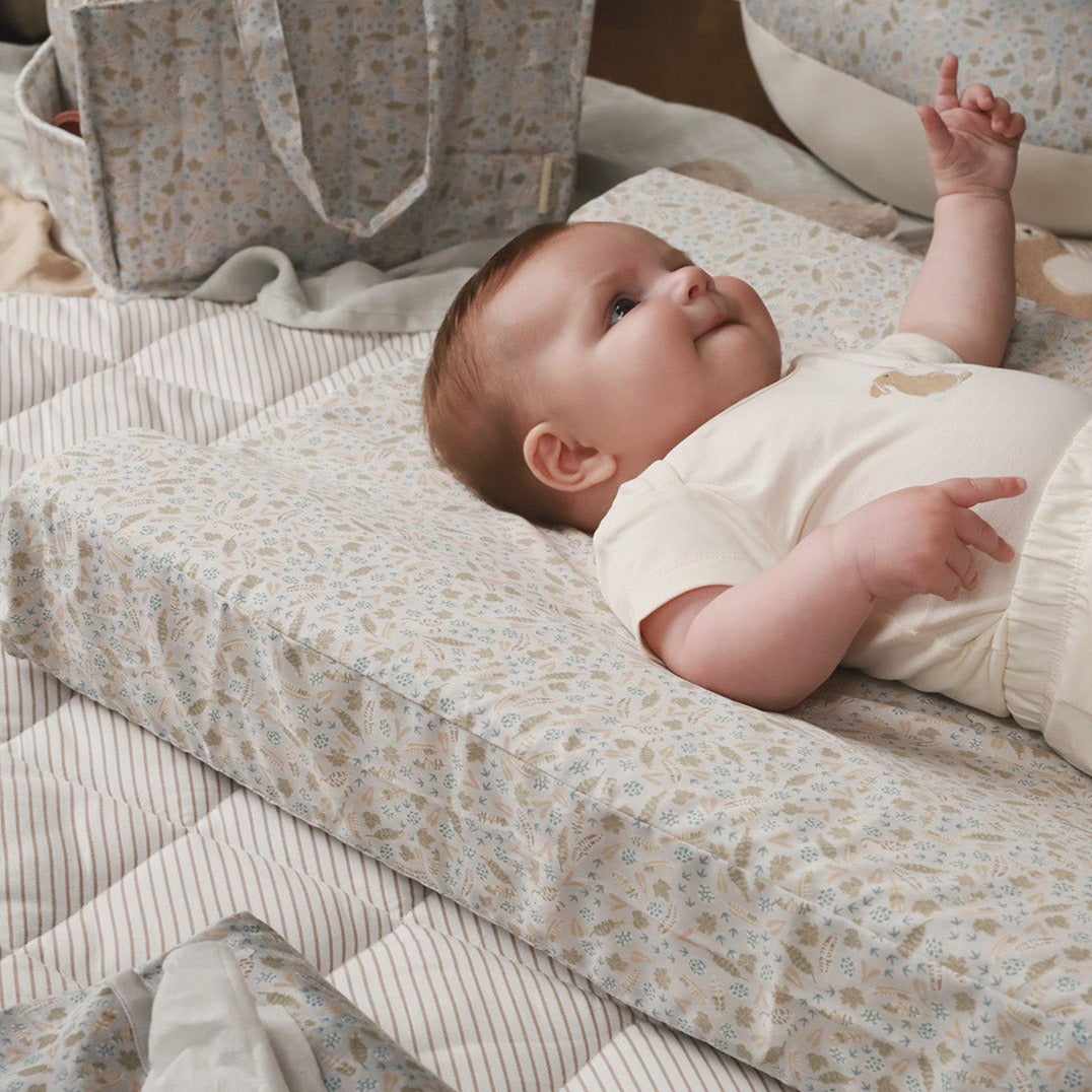 Baby lying on a floral-patterned mattress with a neutral background