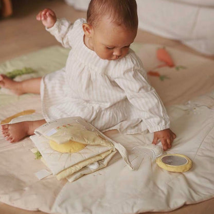 Baby in white outfit playing with a yellow toy on a bed