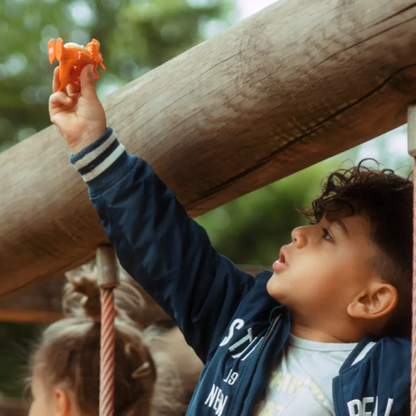 Child holding an orange toy on a playground structure with greenery in the background