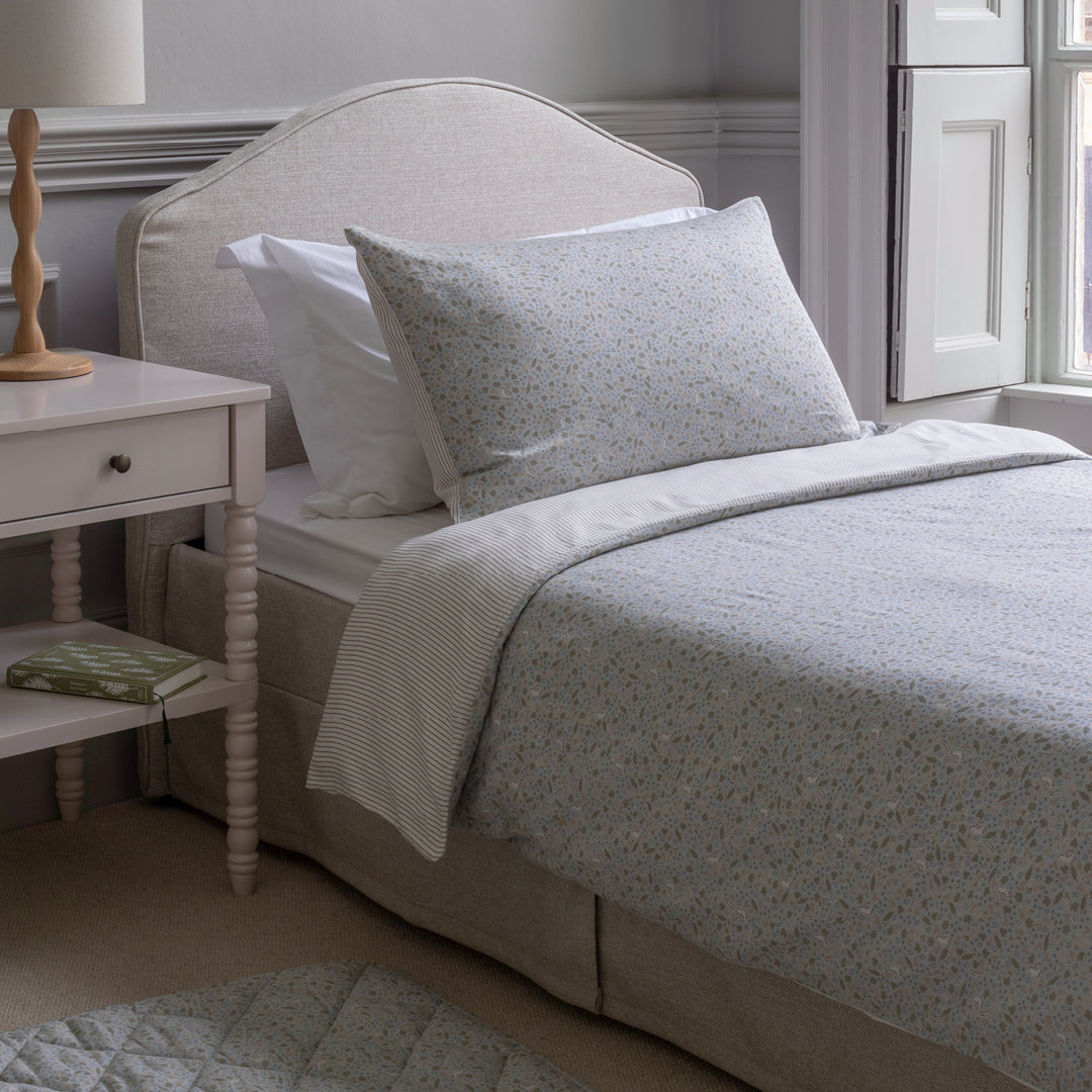 Neatly made bed with light gray bedding in a bedroom setting.