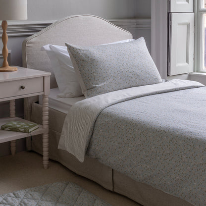 Neatly made bed with light gray bedding in a bedroom setting.