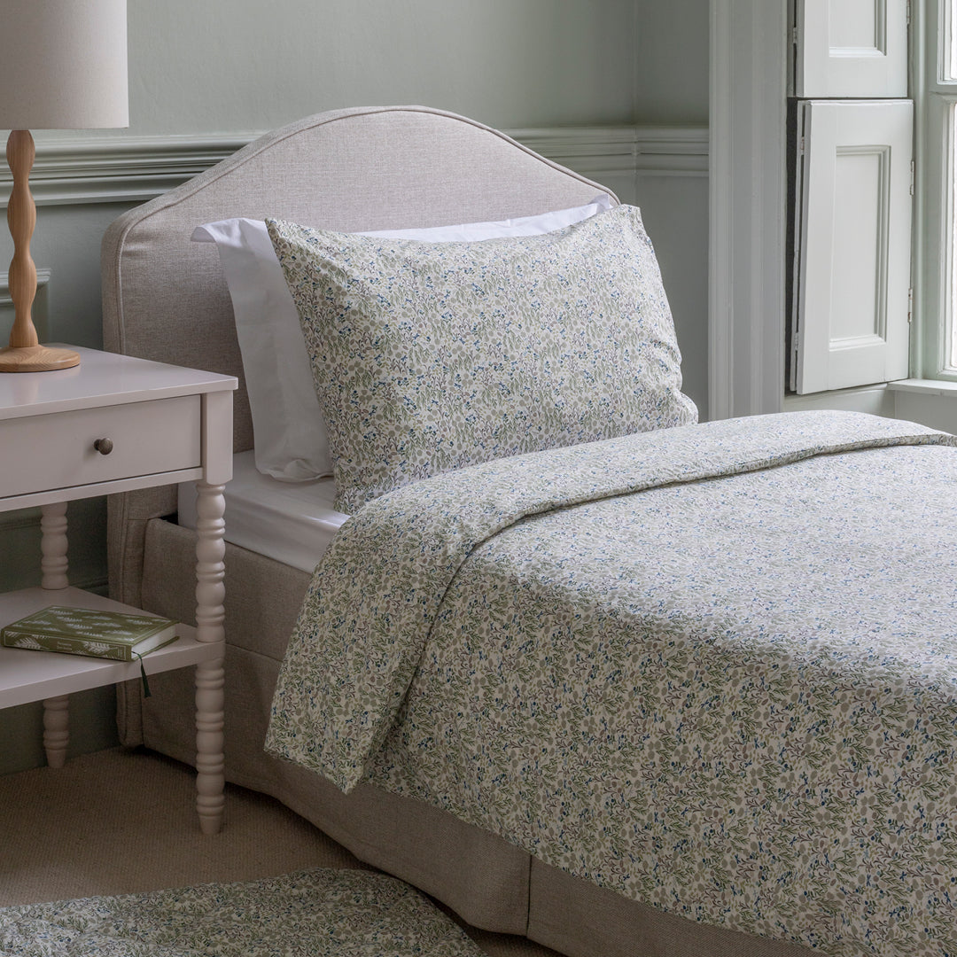 Floral-patterned bedding on a bed in a bedroom setting with a side table.