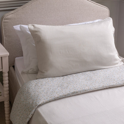 Neatly made bed with striped pillows and a floral-patterned quilt on a neutral-colored headboard.