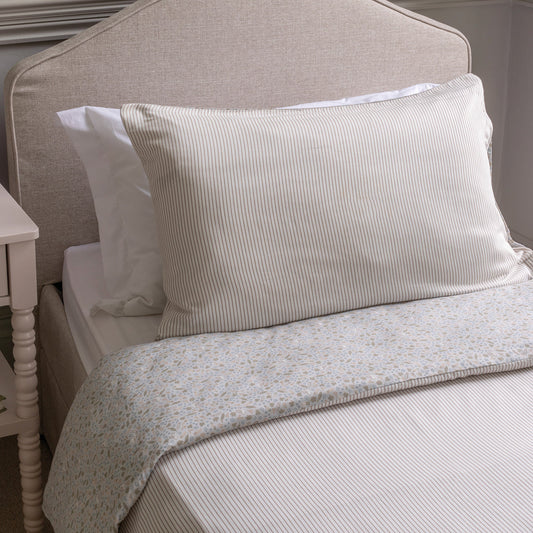 Neatly made bed with striped pillows and a floral-patterned quilt on a neutral-colored headboard.