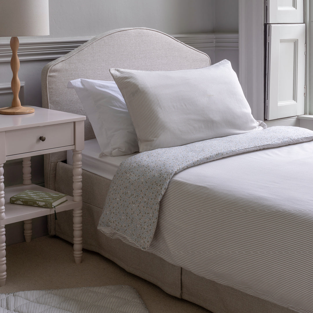 Neatly made bed with white pillows and a light-colored blanket in a bedroom setting.