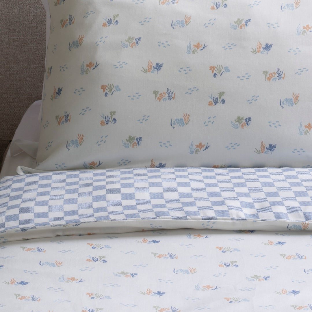 Floral and checkered patterned bed sheets on a bed with a pillow.