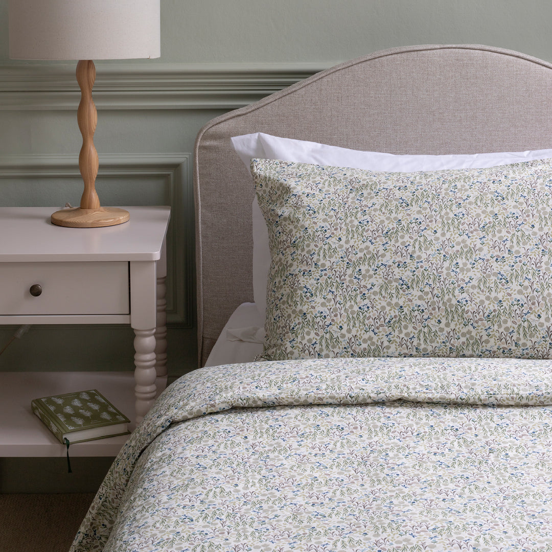Floral bedding set on a bed with a nightstand and lamp in a bedroom setting.