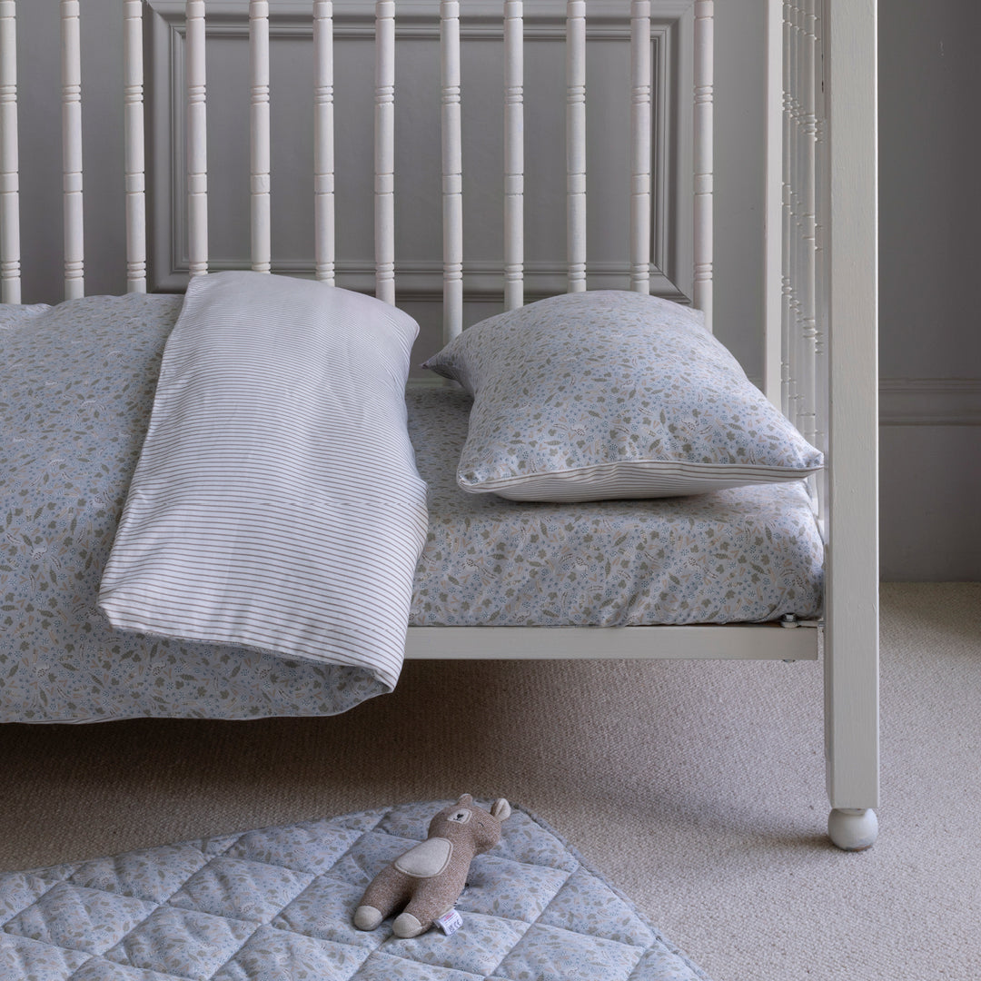 Children's bed with floral bedding and a teddy bear on a quilted mat.